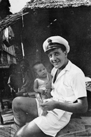 Kenneth Collings with baby in hut on Pacific island